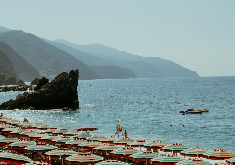 Spiaggia di Fegina a Monterosso al Mare, in Liguria: file di ombrelloni a righe davanti al mare e alla costa