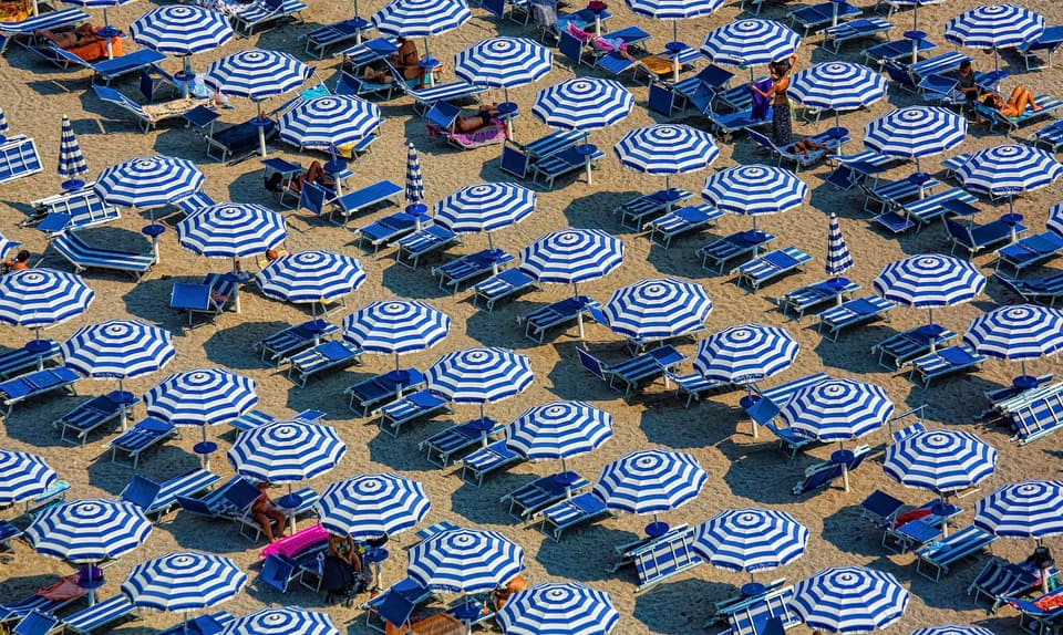 Ombrelloni a righe bianche e blu disposti in file regolari su una spiaggia, visti dall'alto